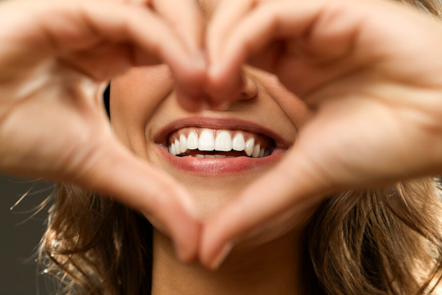 Closeup of a woman making a heart shape with her hands in front of her beautiful white smile