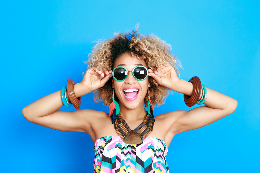 Black woman wearing sunglasses and chunky jewelry smiles after professional teeth whitening in Henderson, NV