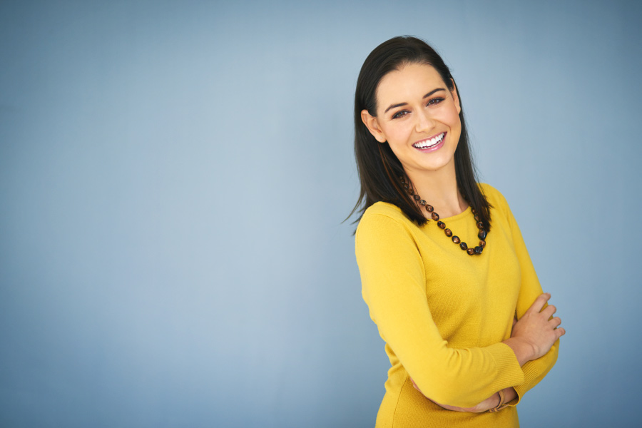 Brunette woman in a yellow shirt smiles after getting a bridge and dental implant tooth replacement in Henderson, NV