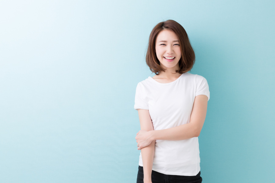 Brunette woman in a white shirt smiles against a blue wall after teeth whitening in Henderson, NV