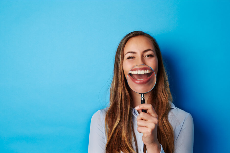 Brunette woman smiles while holding a magnifying glass up to her teeth