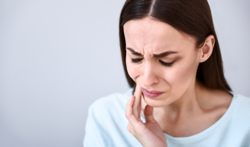 Brunette woman cringes in pain due to a toothache after chewing on hard candy