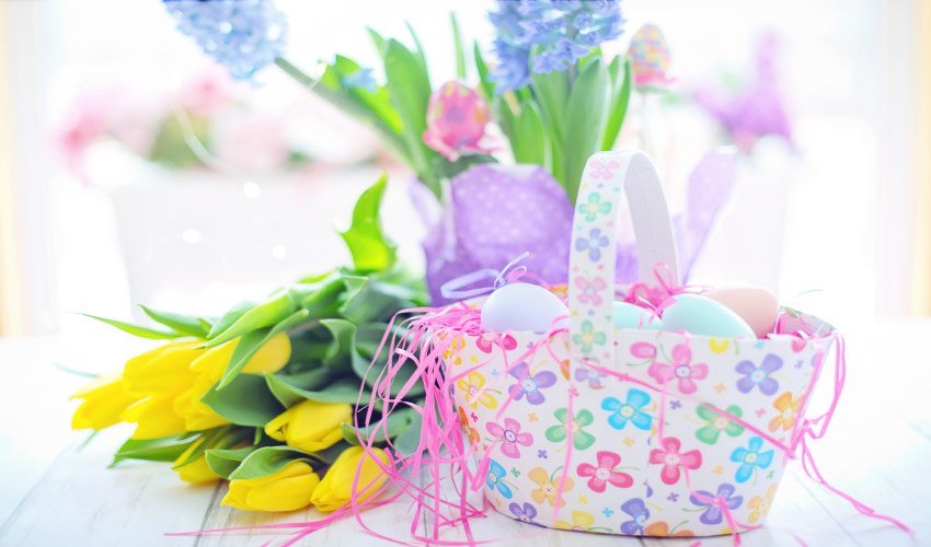 A floral Easter basket with Easter eggs next to a bouquet of yellow tulips