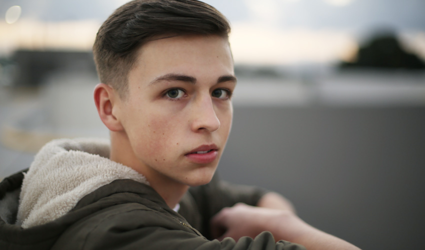 Brunette young man wearing a green jacket at the beach wonders about plaque and tartar on teeth