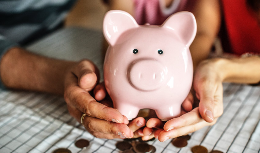 hands holding a piggy bank on top of pennies