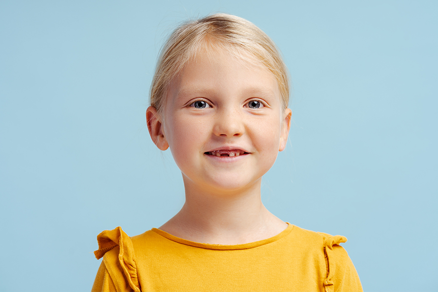 Little girl missing one of her teeth smiles against a blue background